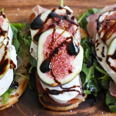 three sandwiches with figs, cheese and sauce on them sitting on a cutting board