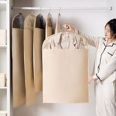 a woman standing in front of a closet holding up a bag with clothes hanging from it