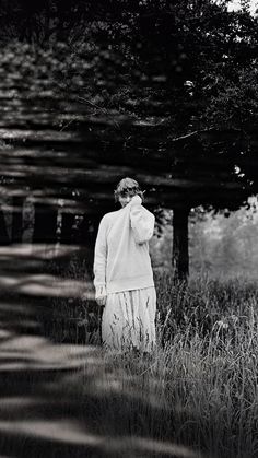 black and white photograph of woman in long dress walking through tall grass with trees behind her