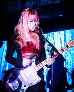 a woman with pink hair playing an electric guitar in front of a microphone on stage