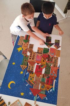 two young boys sitting at a table with paper cut out of the shape of a city