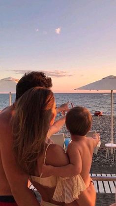 a man holding a baby while sitting on top of a chair next to the ocean