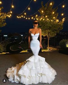 a woman in a white wedding dress standing on a patio with lights strung above her