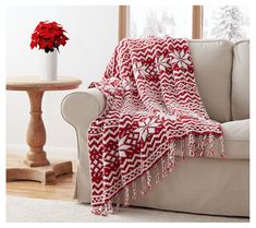 a red and white blanket sitting on top of a couch next to a vase filled with flowers