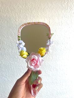 a hand holding a mirror with flowers on it