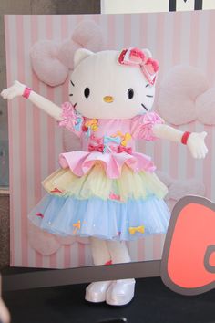 a hello kitty doll is standing in front of a computer screen and holding her arms out