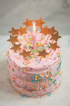 a pink birthday cake with sprinkles and a lit candle