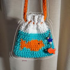 a crocheted purse with an orange and blue fish on the front hanging from a hook