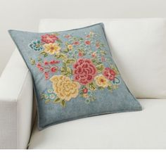 a white couch with a blue pillow on top of it and flowers embroidered on the back