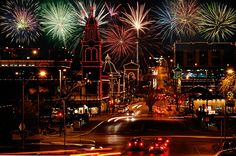 fireworks are lit up in the night sky above a city street with cars driving on it