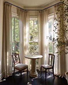 two chairs and a table in front of a window with curtains on the windowsill