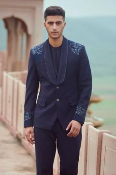 a man in a blue suit stands on a bridge with his hands in his pockets