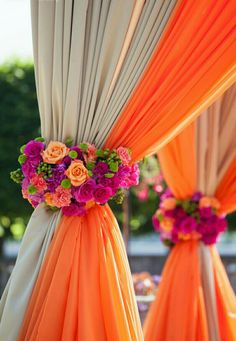 orange and pink flowers are on the back of draping for an outdoor ceremony