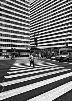 black and white photograph of people crossing the street in front of tall buildings with glass windows