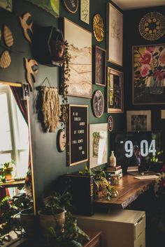 a desk with many pictures and plants on the wall above it, along with a computer