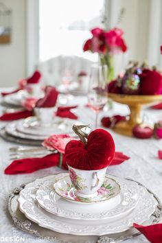 the table is set for valentine's day with red flowers and heart - shaped dishes