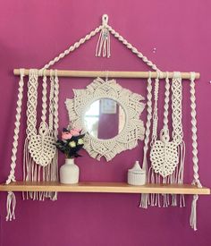 there is a mirror, vase with flowers and macrame hanging on the wall