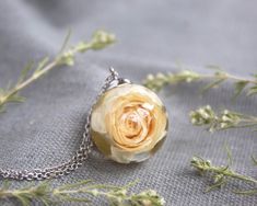 a necklace with a yellow rose on it sitting on top of a gray cloth covered surface