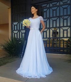 a woman standing in front of a large door holding a bouquet of yellow and white flowers