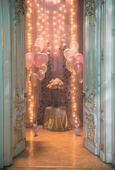 an entrance to a party with balloons and lights on the walls, along with a vase filled with flowers