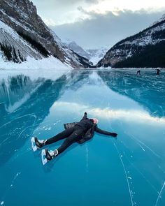 a person laying on the ice in front of some mountains and water with their feet up