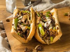 two sandwiches with meat, peppers and onions on a cutting board