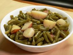 a white bowl filled with green beans and potatoes on top of a wooden table next to a computer keyboard