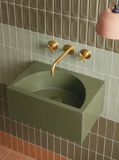 a green sink with two golden faucets on the wall and tiled walls behind it