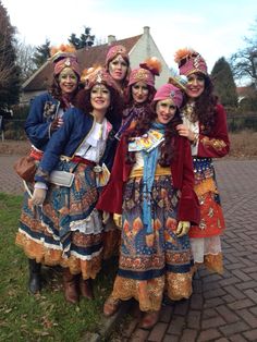 four women dressed in colorful costumes posing for a photo on a brick walkway with their arms around each other