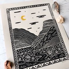 an art print with mountains and trees in the background on a white surface next to some rocks