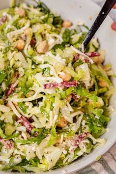 a white bowl filled with salad on top of a table next to a person holding a fork