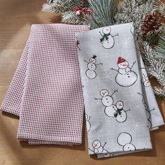 two napkins with snowmen on them sitting next to pine cones and evergreen branches