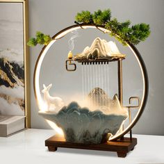 a glass sculpture with a deer and mountain scene in the center, on top of a wooden stand