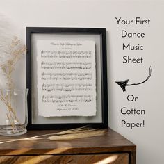 an old sheet music paper is displayed in a frame next to a vase with feathers