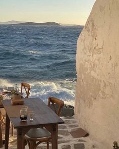 an outdoor dining area overlooking the ocean with wooden chairs and table set for four on stone steps