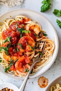 pasta with shrimp and tomato sauce in a white bowl on a marble countertop next to basil leaves