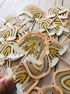 a person is holding up some paper cut out shapes on a table with wood sticks