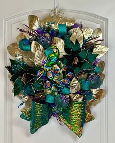 a green and gold wreath hanging on the front door to a white door with an ornate bow