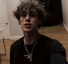 a young man with curly hair wearing a black t - shirt and silver chain necklace