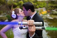 a bride and groom kissing while holding lightsabes