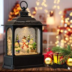 a lantern with snowmen and christmas trees inside on a wooden table next to presents