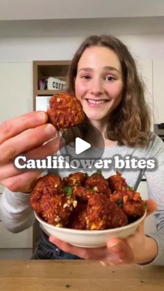 a woman holding a bowl filled with meatballs