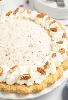 a pie with whipped cream and pecans on top sits on a plate next to other desserts