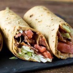 two burritos with meat, lettuce and tomato on a black plate