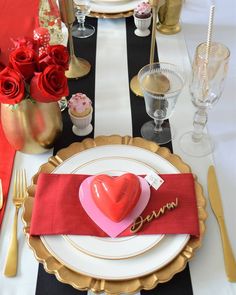 a table set for valentine's day with red and gold place settings, black and white striped napkins