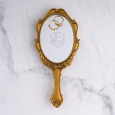 an ornate gold mirror with two wedding rings on it sitting on a marble countertop