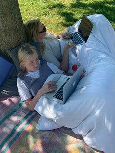 two women laying in the grass with laptops