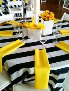 a black and white striped table cloth with yellow napkins, flowers and wine glasses