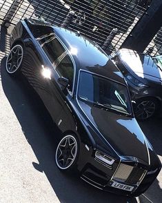 two black cars parked next to each other in front of a fenced off area