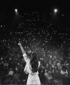 a woman standing on top of a stage holding her arms up in front of an audience